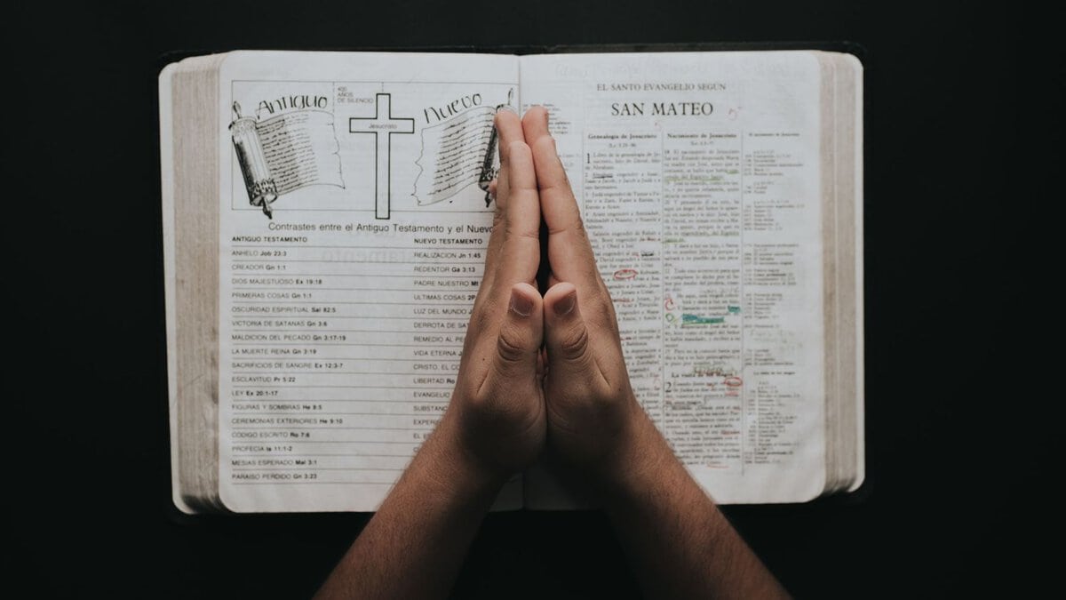 Hands resting in prayer on an open Bible