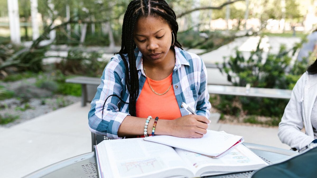 A woman writes in a notebook at an outdoor table.