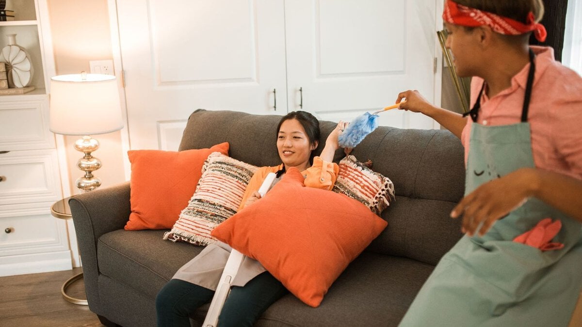 Two people share a playful moment while cleaning beside a couch.