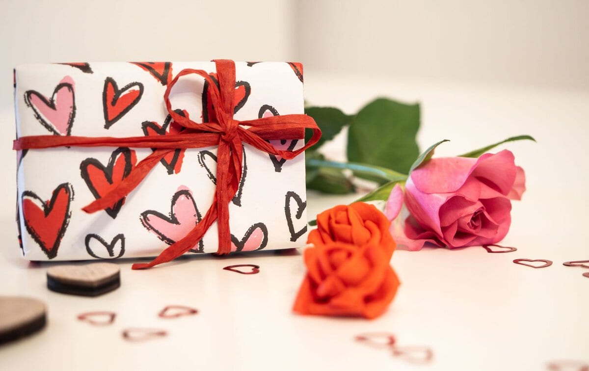 A gift box decorated with hearts beside flowers