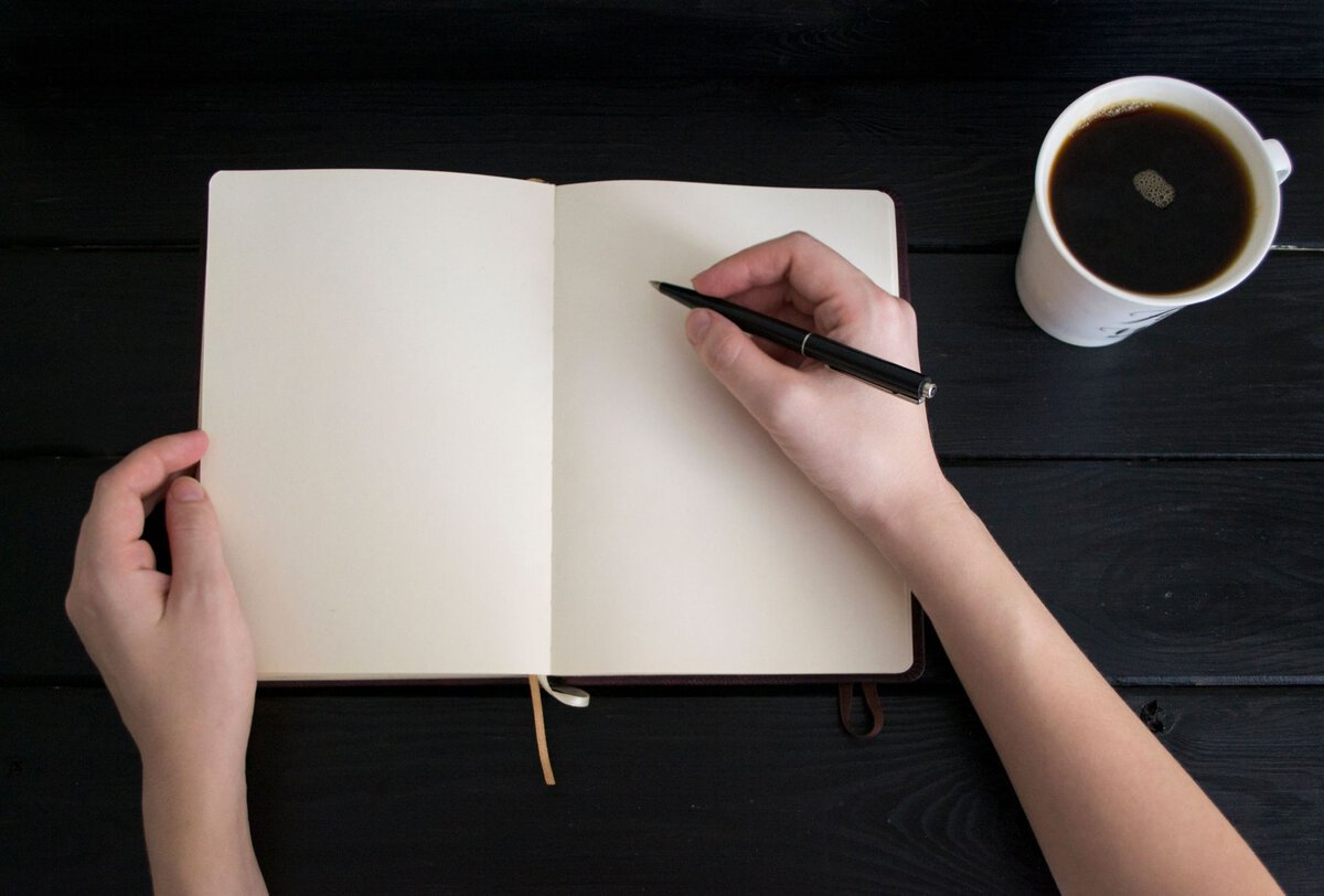Hands writing in an open notebook beside coffee