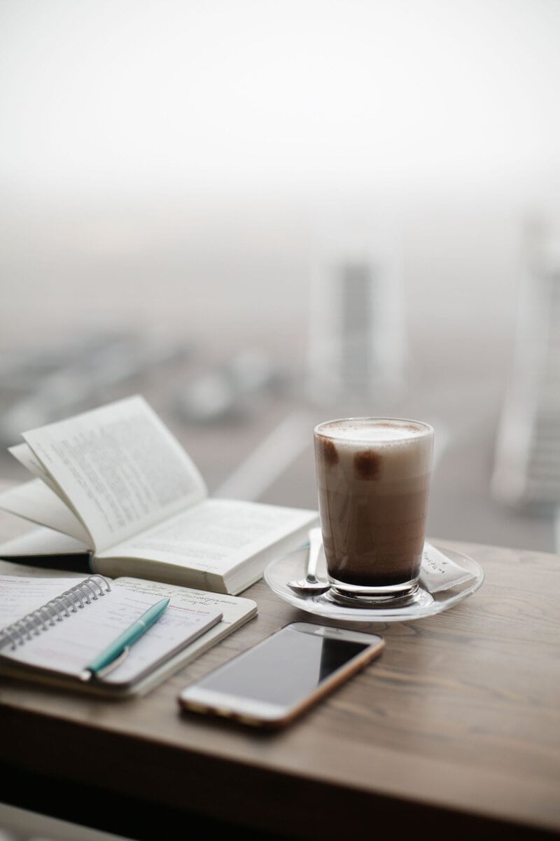 Coffee, an open book and a phone beside a window