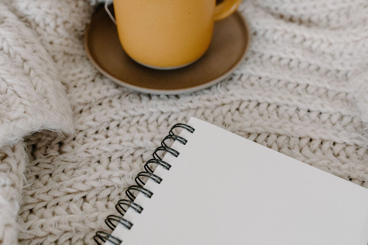 Blank notebook beside a mug on a knitted blanket