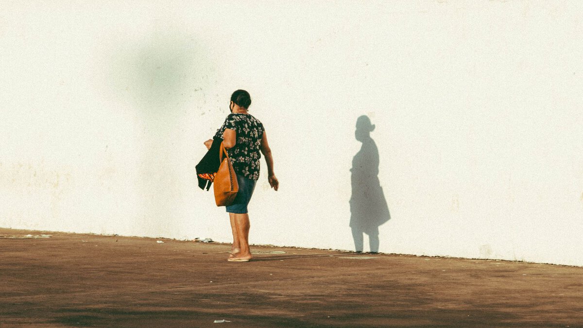 Woman and her shadow beside a sunlit wall