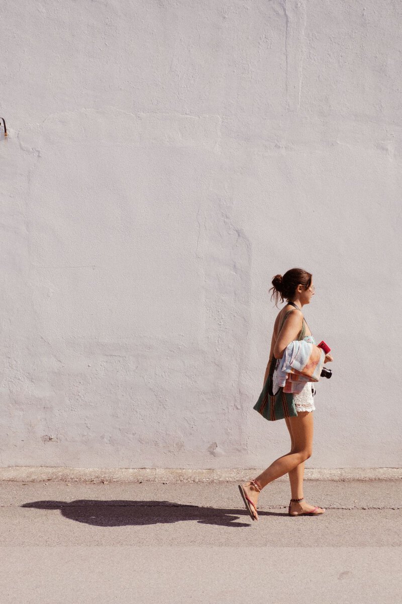Woman walking beside a sunlit white wall
