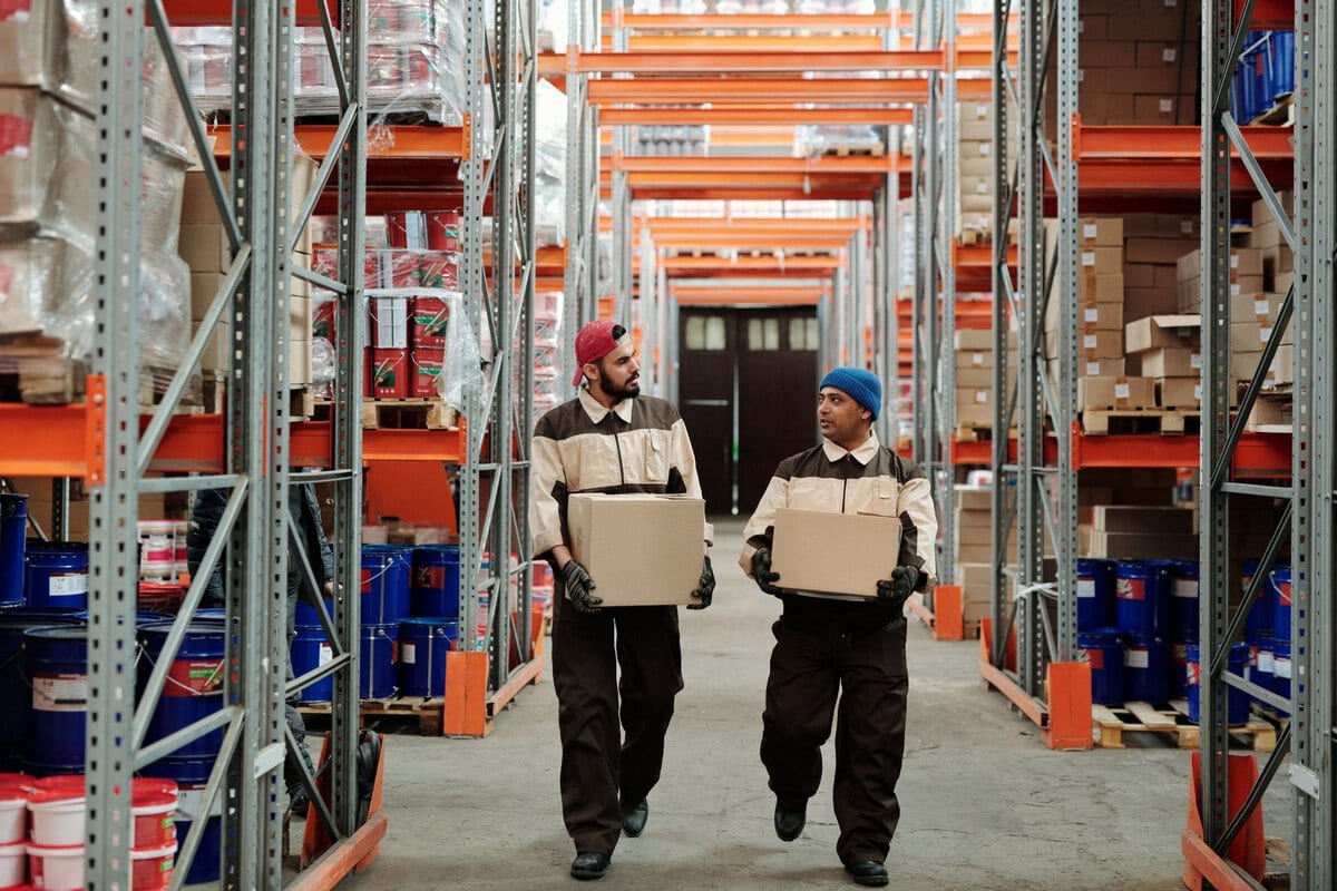 Two workers carrying boxes in a warehouse aisle