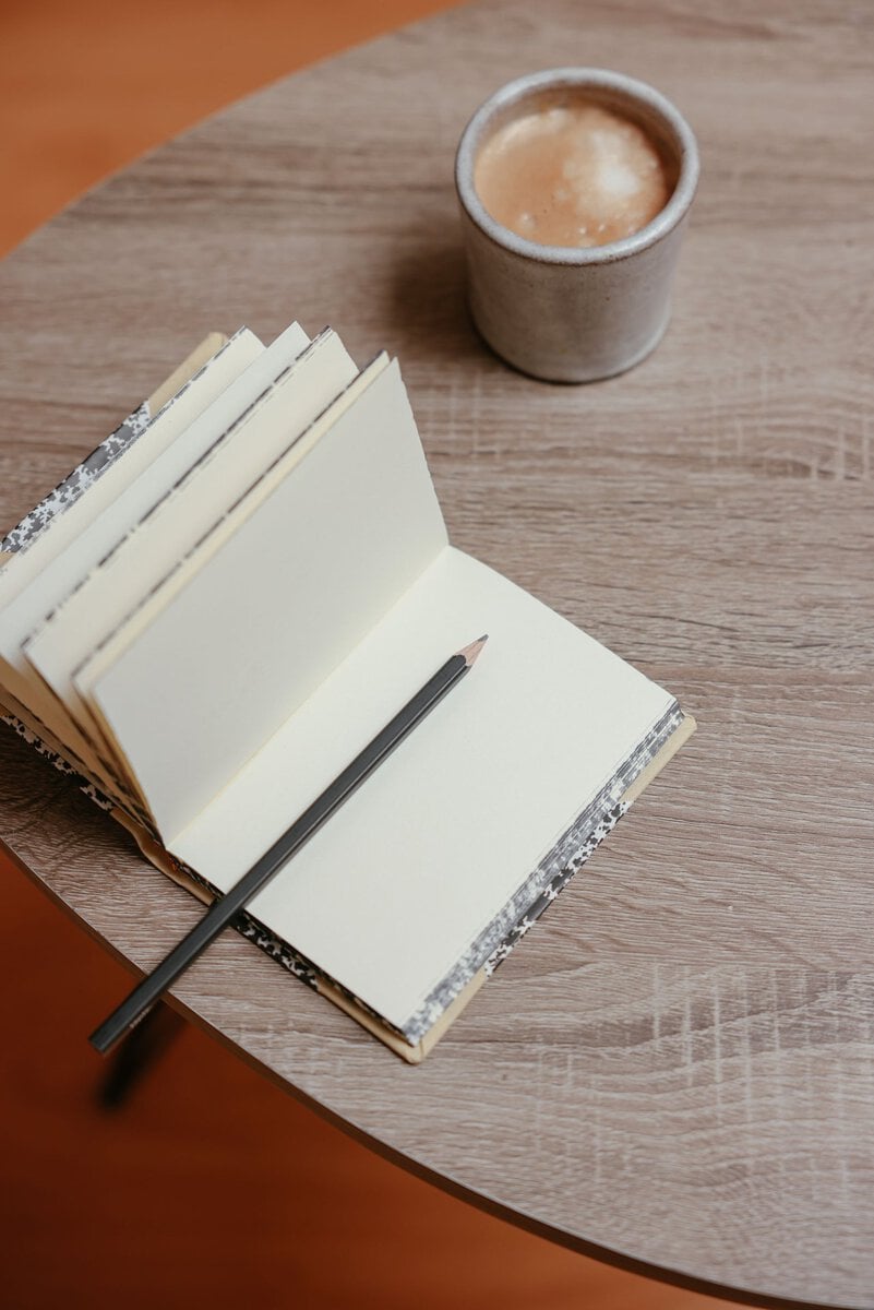 Open notebook and pencil beside a cup of coffee