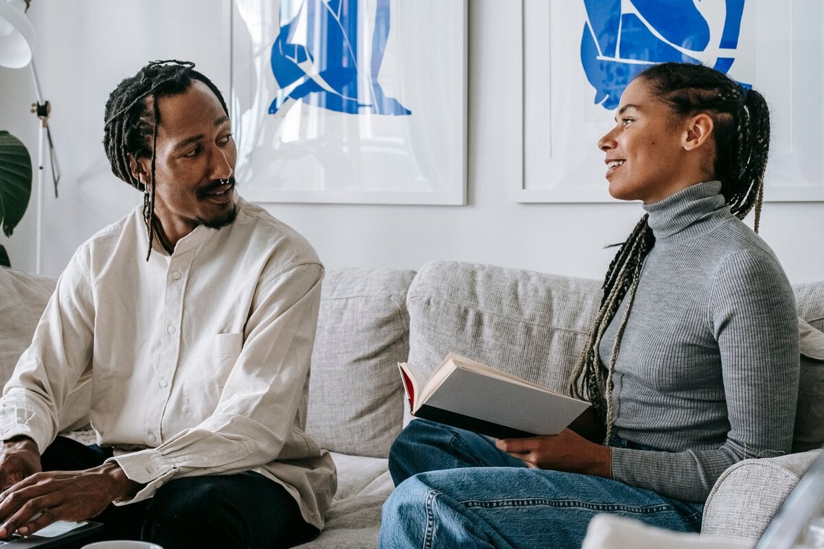 Couple talking at home with a book and laptop
